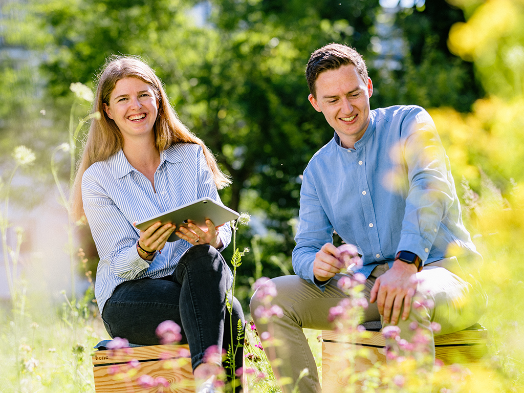 Two MorgenGrün employees sitting in a green outdoor setting and laughing