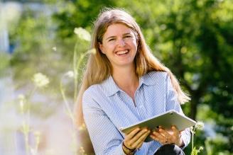 Foto einer MorgenGrün-Mitarbeiterin mit Tablet in grüner Natur bei der Arbeit in einer entspannten Umgebung