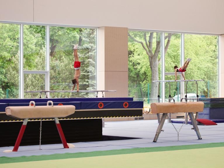 Innenaufnahme einer modernen Turnhalle im olympischen und paralympischen Trainingszentrum in Grünheide. Große Fenster und schöner Ausblick auf die Natur.  Realisierung eines klimaneutralen Energiekonzeptes für das Trainingszentrum.