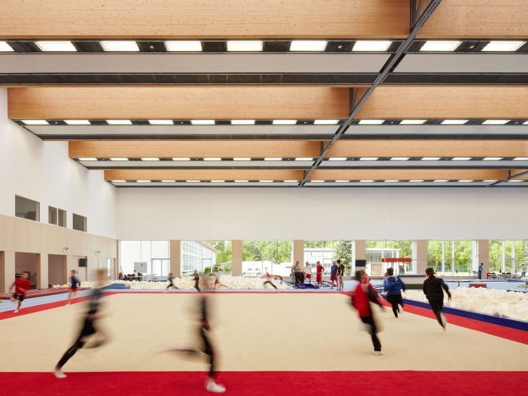 Innenaufnahme einer großen Turnhalle des olympischen und paralympischen Trainingszentrums in Grünheide. Das Bild zeigt, wie sich mehrere Personen in der Halle sportlich betätigen.  Sanierung und Wärmeschutz des Innenraums durch ein klimaneutrales Energiekonzept