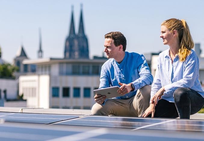 Foto von zwei Personen auf einem Dach mit einer Photovoltaik-Anlage bei der gemeinsamen Arbeit in urbaner Umgebung